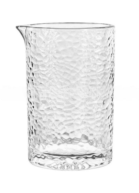 A clear glass mixing glass with a geometric pattern and a brown liquid inside, alongside an empty glass with a geometric pattern.