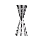 A stainless steel jigger with floral engravings on the side, featuring a narrow waist and additional notches for measurement | Cocktail Ceremony