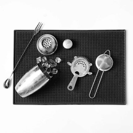 Bar tools including a jigger, strainer, and shaker on a black bar mat.