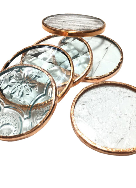 Set of four round glass coasters with copper rims on a white background