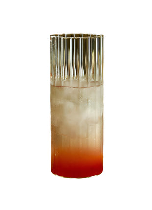 Glass of red and white cocktail with a bottle on a wooden cutting board.