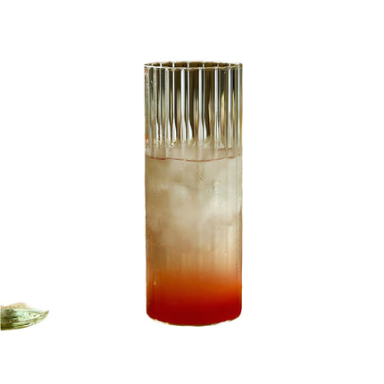 Glass of red and white cocktail with a bottle on a wooden cutting board.