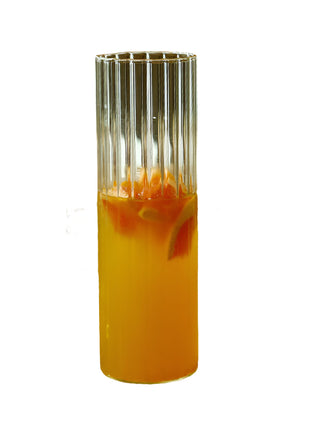 Clear glass with orange juice on a wooden tray with a bottle of water and pastries in the background.