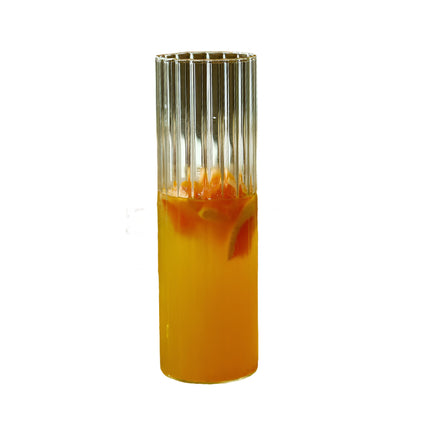 Clear glass with orange juice on a wooden tray with a bottle of water and pastries in the background.